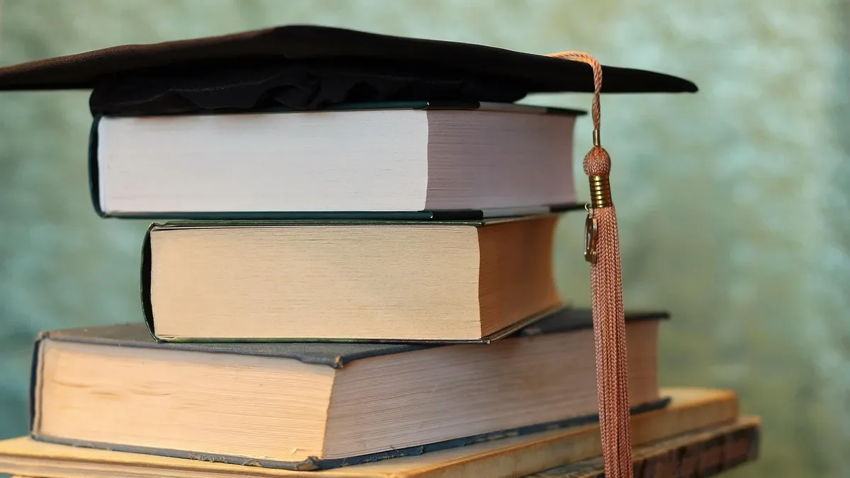 A stack of books topped with a graduation cap.